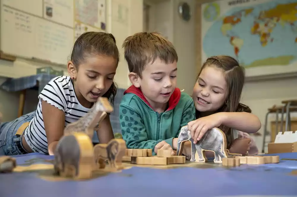 Preschool children working with a wooden moveable alphabet on a mat in a sunlit Montessori classroom